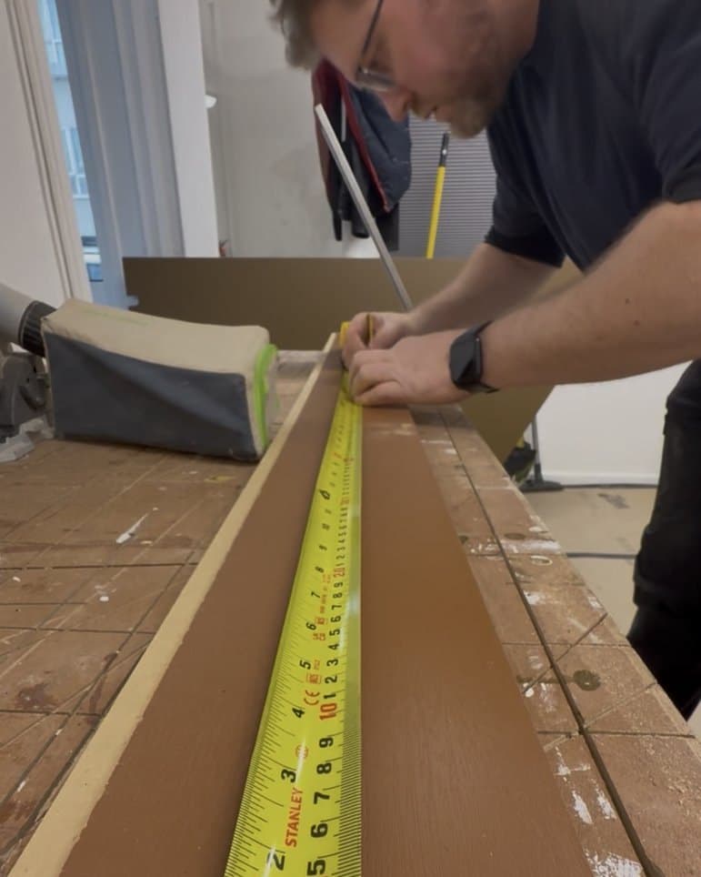 Rafal marking out a board with a pencil and a tape measure on his workbench